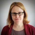 head shot portrait of Idit Dvir, a white woman with blonde hair, black framed glasses wearing a red sweater